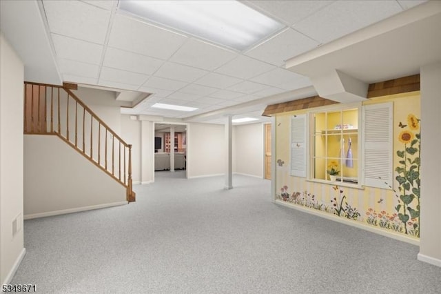 finished basement with carpet floors, baseboards, stairs, and a paneled ceiling