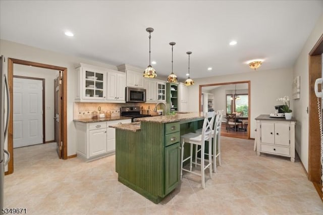 kitchen featuring green cabinetry, stainless steel appliances, white cabinets, an island with sink, and a breakfast bar
