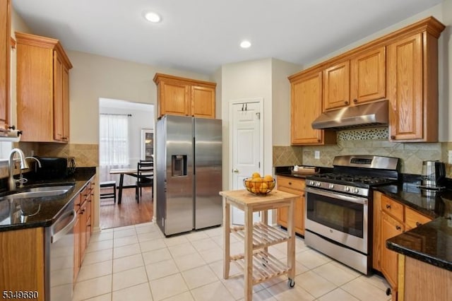 kitchen featuring tasteful backsplash, a sink, under cabinet range hood, dark stone counters, and stainless steel appliances
