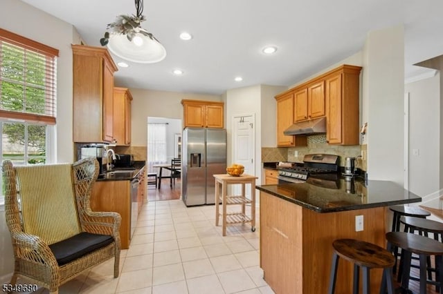 kitchen featuring appliances with stainless steel finishes, a sink, a peninsula, tasteful backsplash, and under cabinet range hood