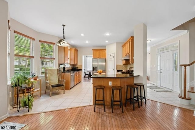 kitchen with dark countertops, tasteful backsplash, a peninsula, under cabinet range hood, and stainless steel appliances