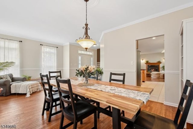 dining space featuring crown molding, wood finished floors, and a lit fireplace