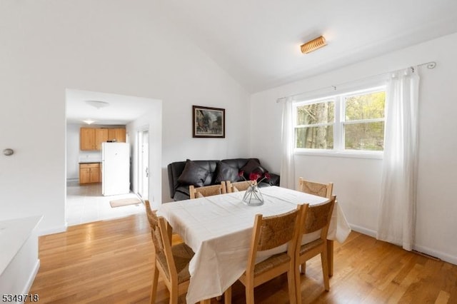 dining area with light wood finished floors, baseboards, and high vaulted ceiling