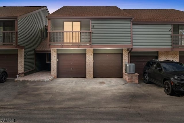townhome / multi-family property featuring driveway, brick siding, a balcony, an attached garage, and a shingled roof