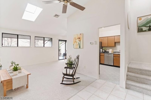 living area featuring a ceiling fan, visible vents, a skylight, high vaulted ceiling, and light carpet
