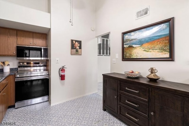 kitchen with visible vents, brown cabinetry, dark countertops, baseboards, and appliances with stainless steel finishes