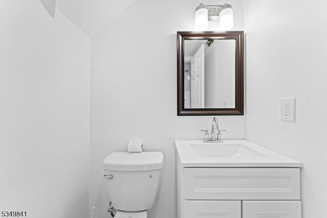 half bathroom with vanity, toilet, and lofted ceiling