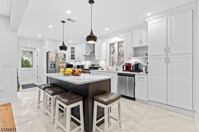 kitchen featuring visible vents, wall chimney exhaust hood, appliances with stainless steel finishes, marble finish floor, and a breakfast bar area