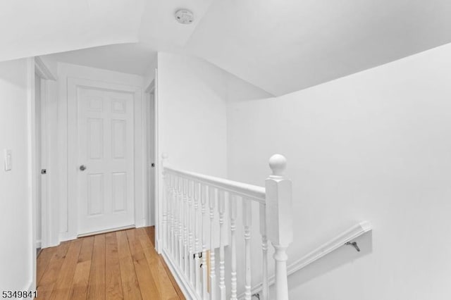 hall with light wood-type flooring, lofted ceiling, and an upstairs landing