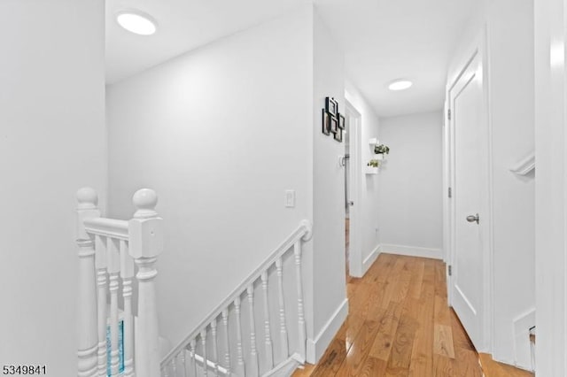 hall featuring an upstairs landing, light wood-style floors, and baseboards