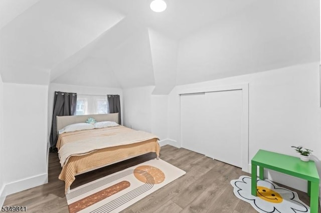 bedroom featuring a closet, baseboards, vaulted ceiling, and wood finished floors