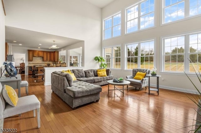 living area featuring wood-type flooring, baseboards, plenty of natural light, and a towering ceiling