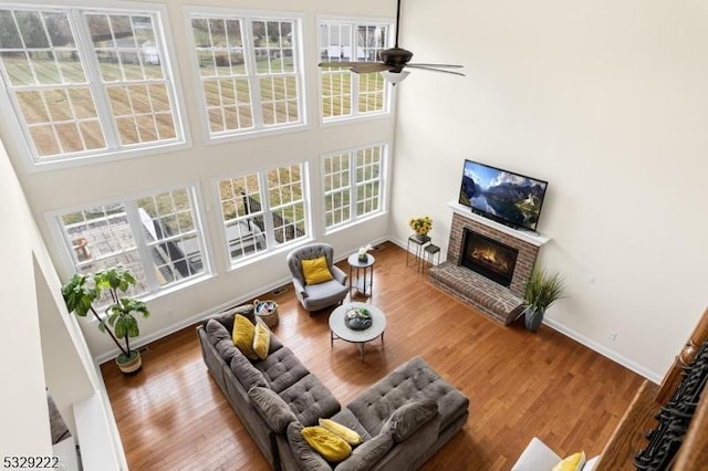 living area featuring baseboards, a ceiling fan, wood finished floors, and a brick fireplace