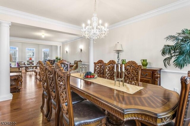 dining area featuring crown molding, wood finished floors, decorative columns, and a notable chandelier