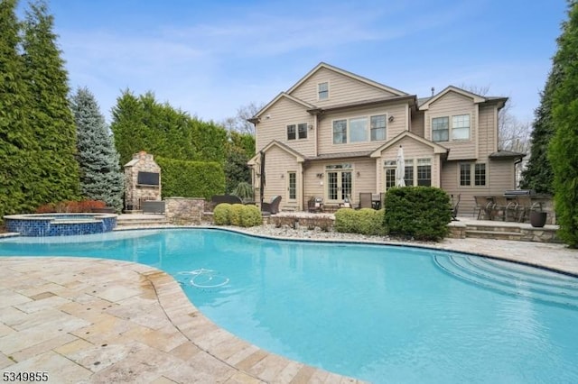 view of swimming pool with a fireplace, a pool with connected hot tub, a patio area, and french doors