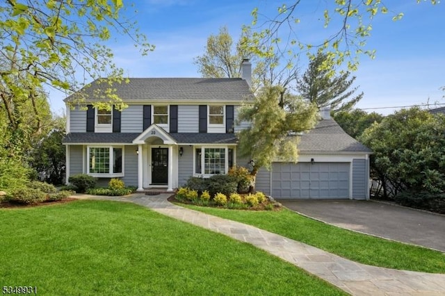 view of front of house with an attached garage, a front yard, driveway, and a chimney