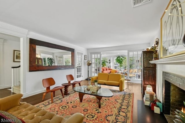 living area with baseboards, a warm lit fireplace, visible vents, and wood finished floors