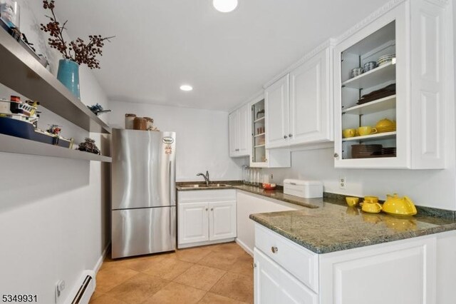 kitchen with freestanding refrigerator, glass insert cabinets, white cabinetry, a baseboard heating unit, and a sink