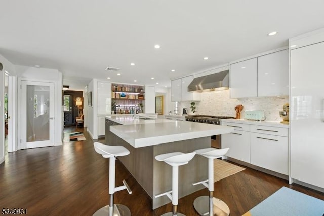 kitchen with range with gas stovetop, modern cabinets, wall chimney exhaust hood, white cabinets, and backsplash
