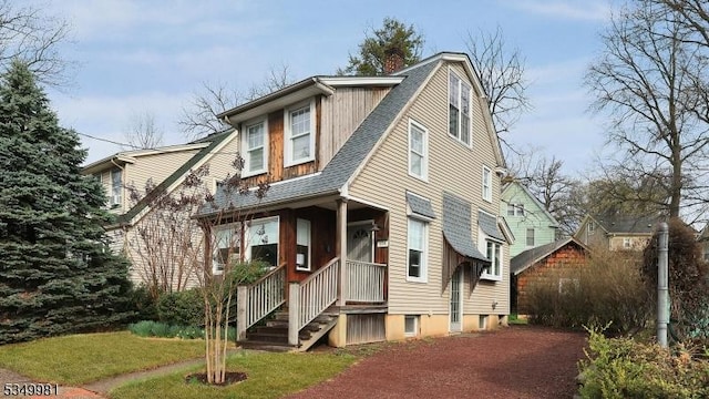 view of front facade with a gambrel roof, a shingled roof, covered porch, and a chimney