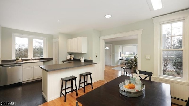 kitchen with white cabinets, a peninsula, dishwasher, and dark countertops