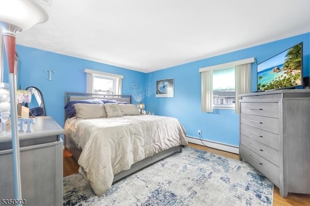 bedroom with a baseboard radiator, multiple windows, and wood finished floors