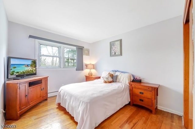 bedroom with a baseboard heating unit, light wood-style flooring, and baseboards