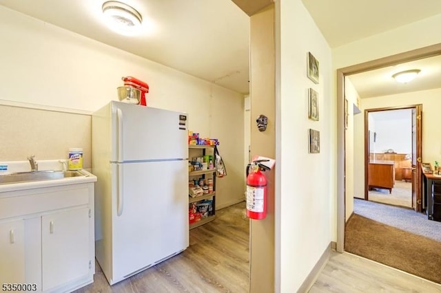 kitchen featuring freestanding refrigerator, light wood-style flooring, light countertops, and a sink