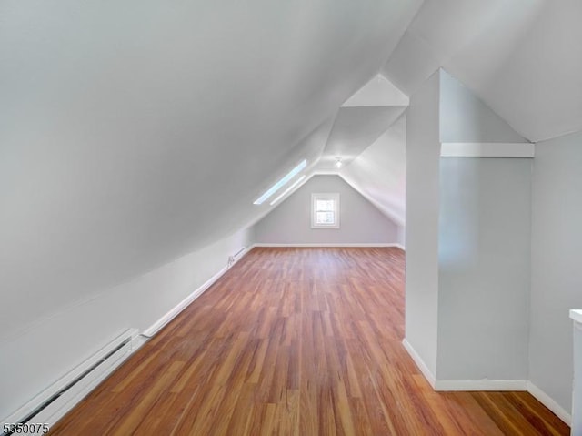 additional living space with baseboards, a baseboard heating unit, vaulted ceiling, and wood finished floors