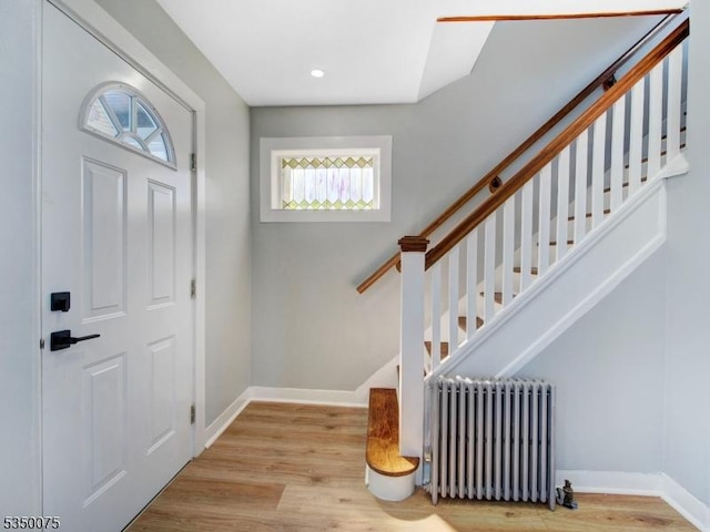 foyer entrance with radiator, wood finished floors, baseboards, and stairs