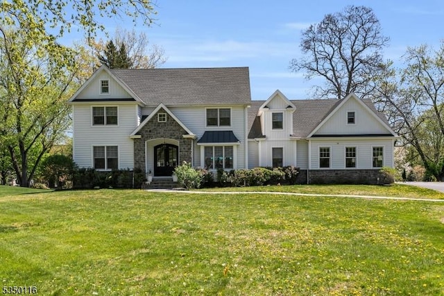 view of front of house with a shingled roof, a front lawn, board and batten siding, and stone siding
