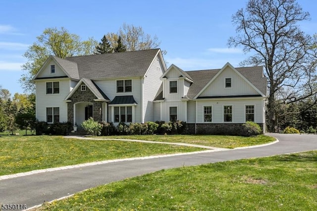 view of front of property with board and batten siding, a front yard, a shingled roof, and stone siding