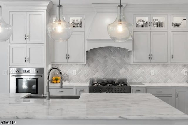 kitchen featuring light stone countertops, a sink, stainless steel oven, gas range, and backsplash