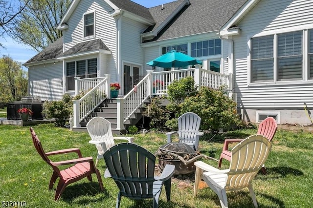rear view of property featuring roof with shingles, stairs, a wooden deck, a lawn, and a fire pit