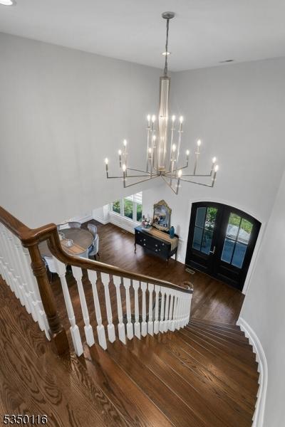 stairs with french doors, wood finished floors, and a notable chandelier