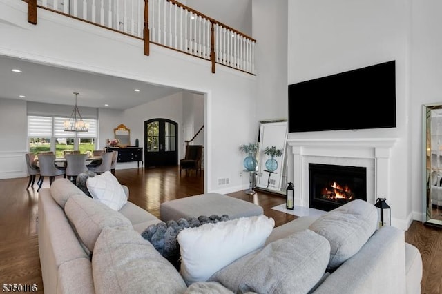 living room with an inviting chandelier, stairs, a fireplace with flush hearth, wood finished floors, and visible vents