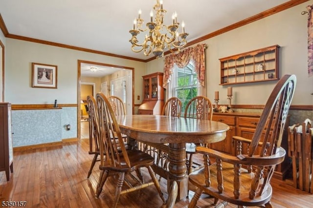 dining space featuring wood-type flooring, a wainscoted wall, ornamental molding, a chandelier, and baseboards