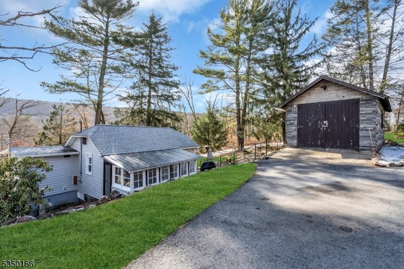 view of side of home featuring a yard, a detached garage, an outdoor structure, a shingled roof, and driveway