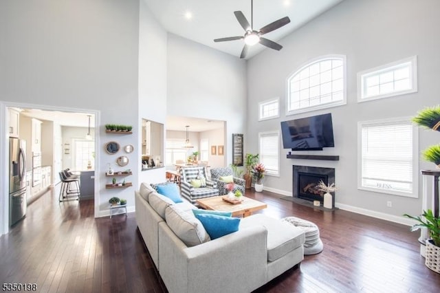 living room featuring high vaulted ceiling, a fireplace with flush hearth, dark wood-style floors, and a ceiling fan