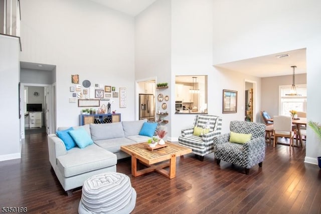 living area featuring wood-type flooring, a towering ceiling, baseboards, and visible vents