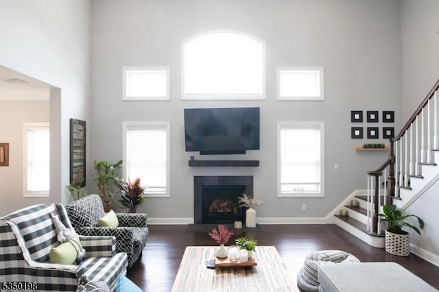 living room with a fireplace with flush hearth, stairway, a towering ceiling, and wood finished floors