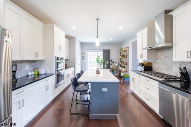 kitchen with appliances with stainless steel finishes, wall chimney exhaust hood, white cabinetry, and a kitchen island