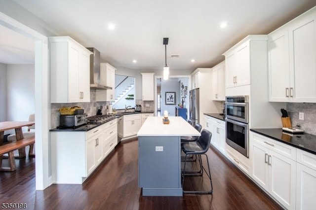 kitchen with white cabinets, wall chimney exhaust hood, decorative backsplash, stainless steel appliances, and a sink