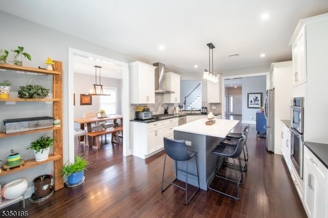 kitchen with white cabinetry, a kitchen island, wall chimney exhaust hood, decorative backsplash, and stainless steel appliances