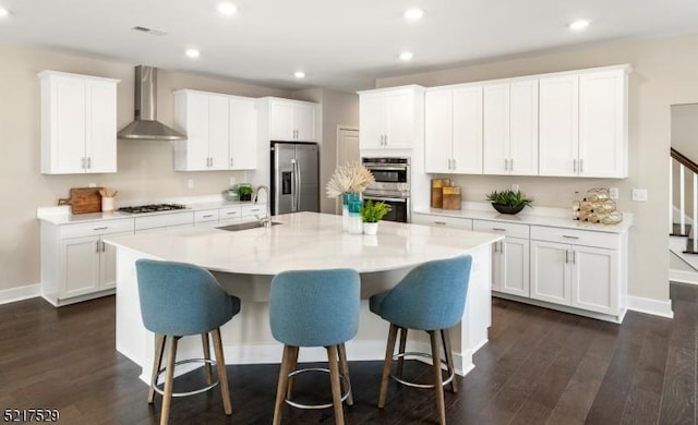kitchen featuring dark wood-type flooring, appliances with stainless steel finishes, a sink, and wall chimney range hood