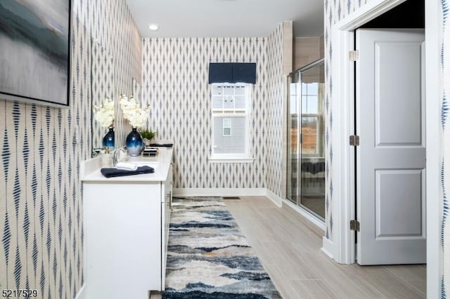 full bathroom featuring vanity, baseboards, wallpapered walls, a shower stall, and wood finished floors