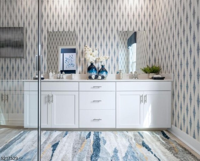 full bathroom featuring wallpapered walls, double vanity, a sink, and baseboards