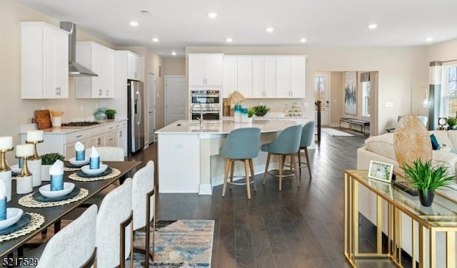 kitchen with a sink, wall chimney range hood, light countertops, appliances with stainless steel finishes, and a breakfast bar