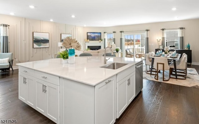 kitchen featuring open floor plan, white cabinetry, dark wood-type flooring, stainless steel dishwasher, and a sink
