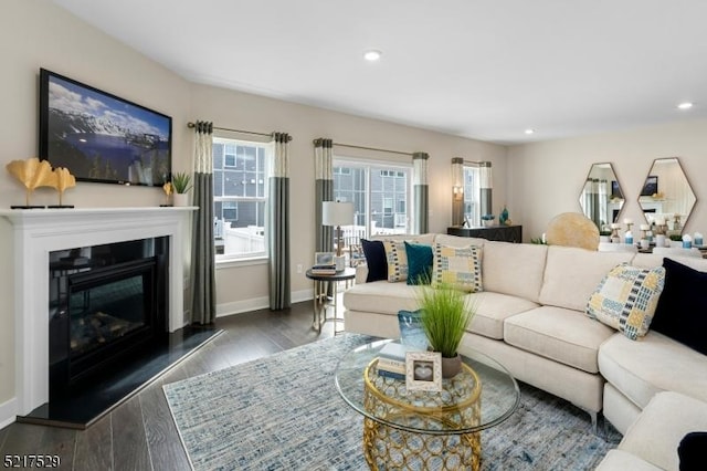 living room featuring a glass covered fireplace, recessed lighting, baseboards, and wood finished floors